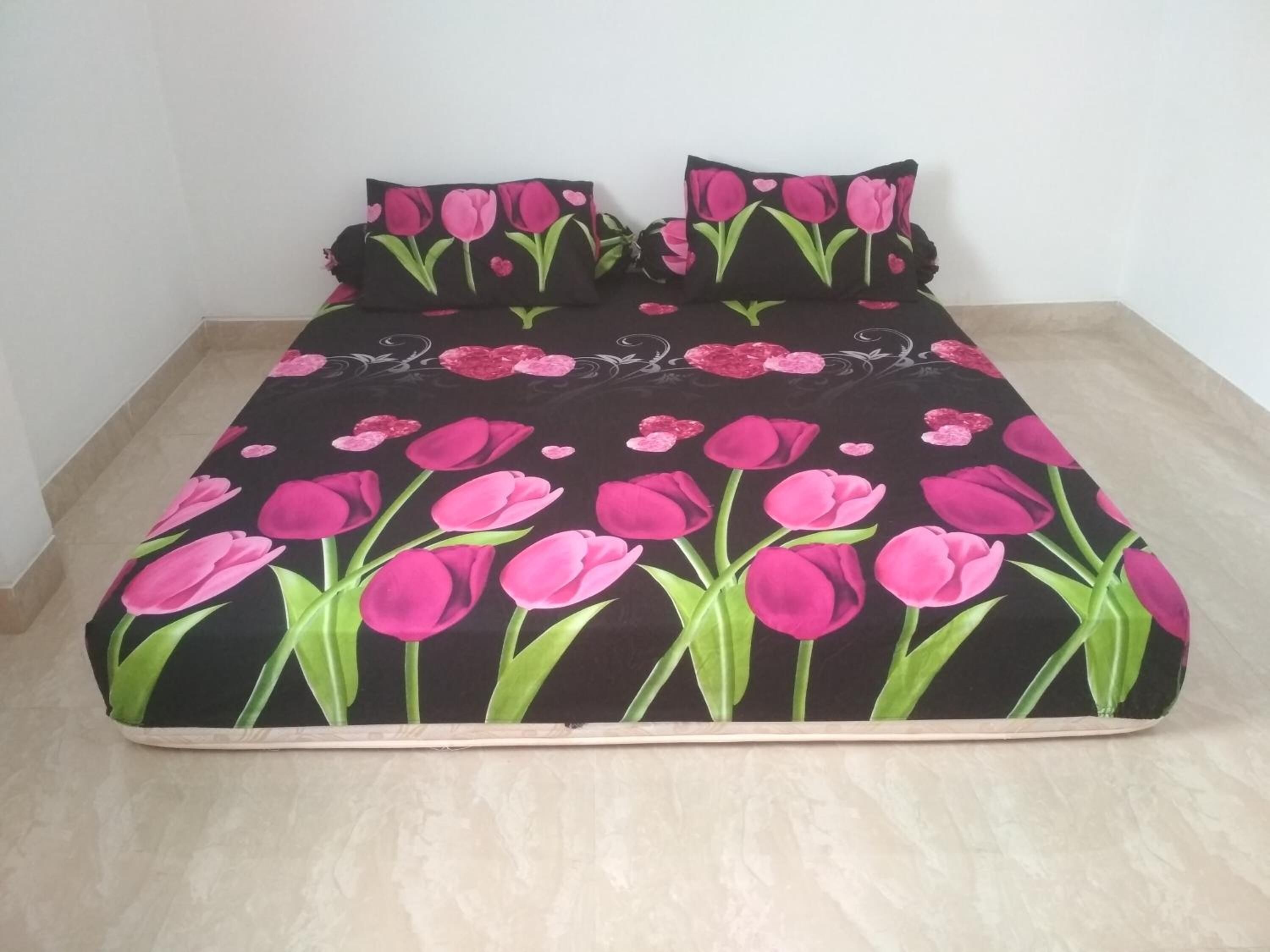 A bed with a black bedspread featuring pink tulips and green leaves.
