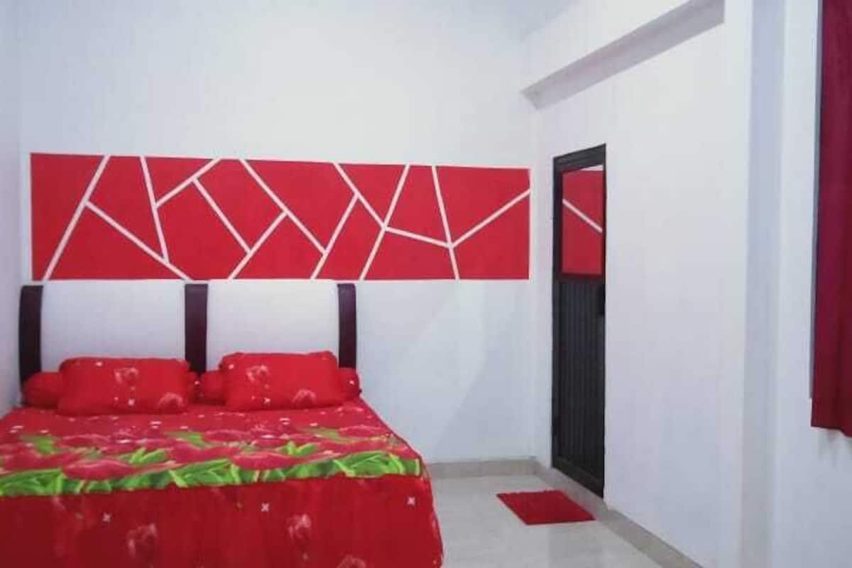 A bedroom with a bed, red bedding, a geometric wall design, and a red curtain.