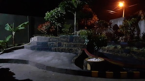 A nighttime outdoor area with a stone staircase, a small water feature, and various plants. - Almira Homestay (Jambi)
