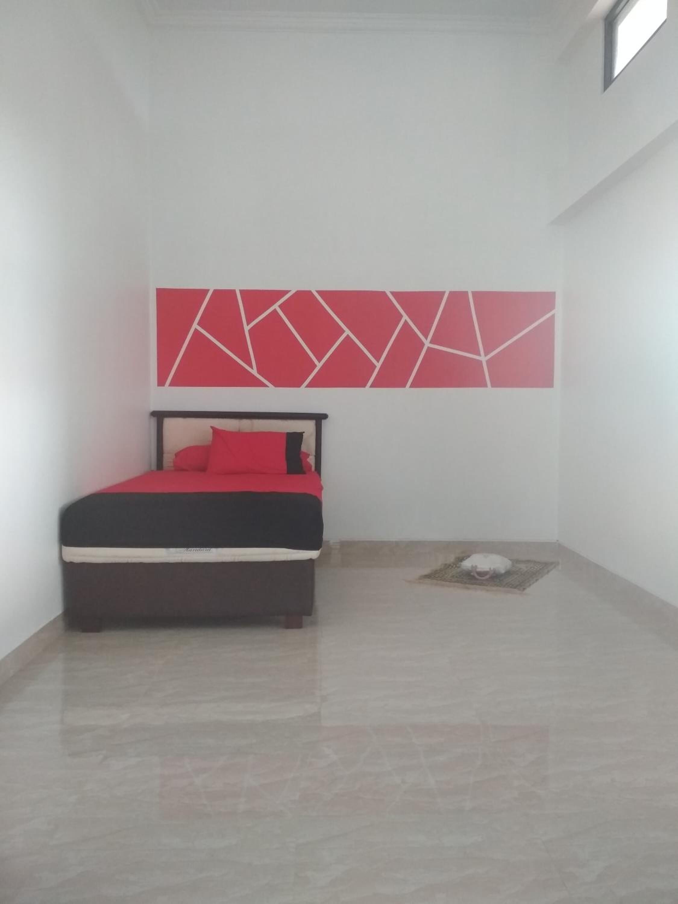 A bedroom with a bed, a red and black headboard, a red geometric wall decoration, and a small rug.