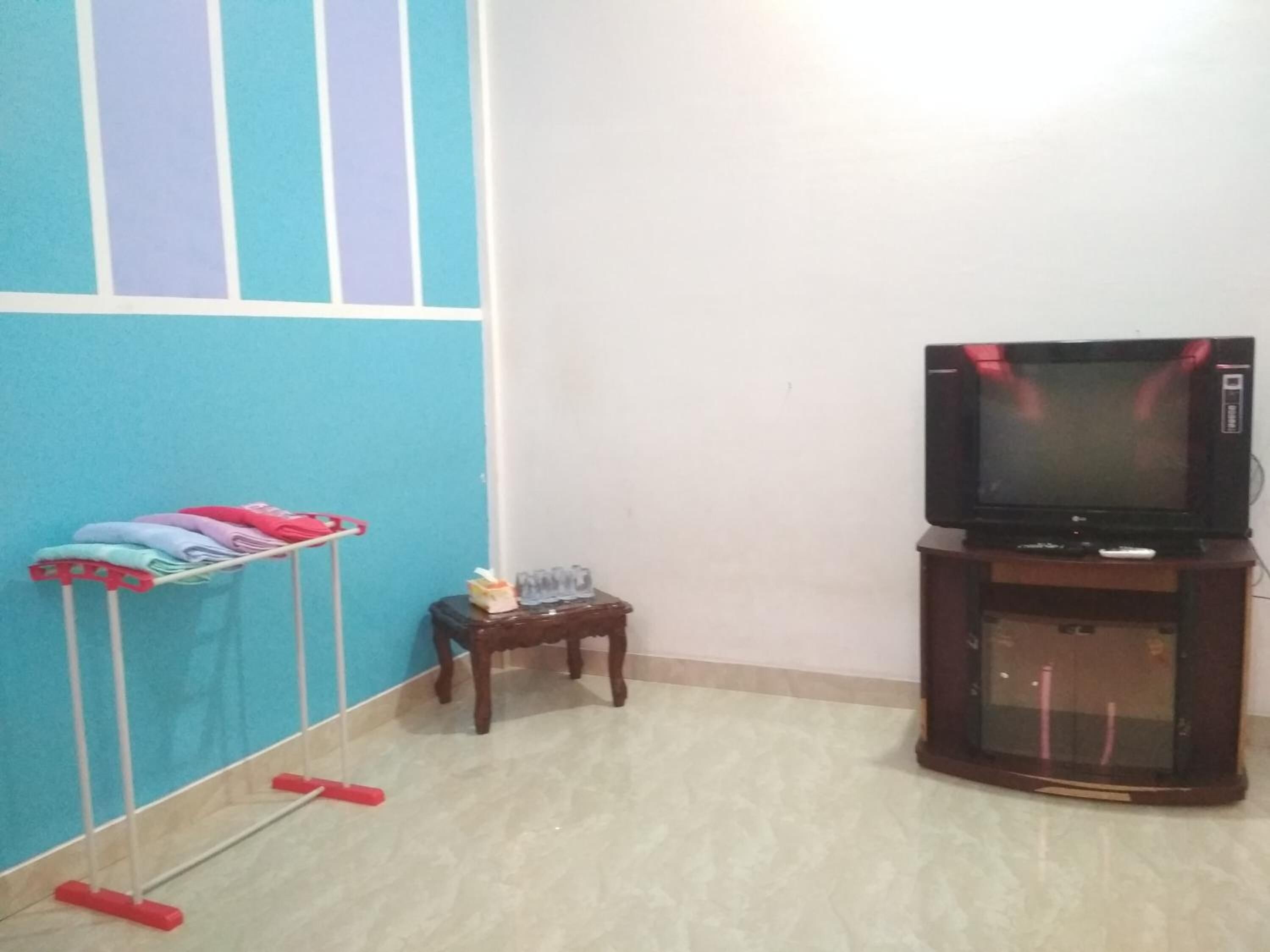 Un salon avec un téléviseur posé sur un meuble, une petite table sur laquelle se trouvent divers objets, et une serpillière appuyée contre le mur.