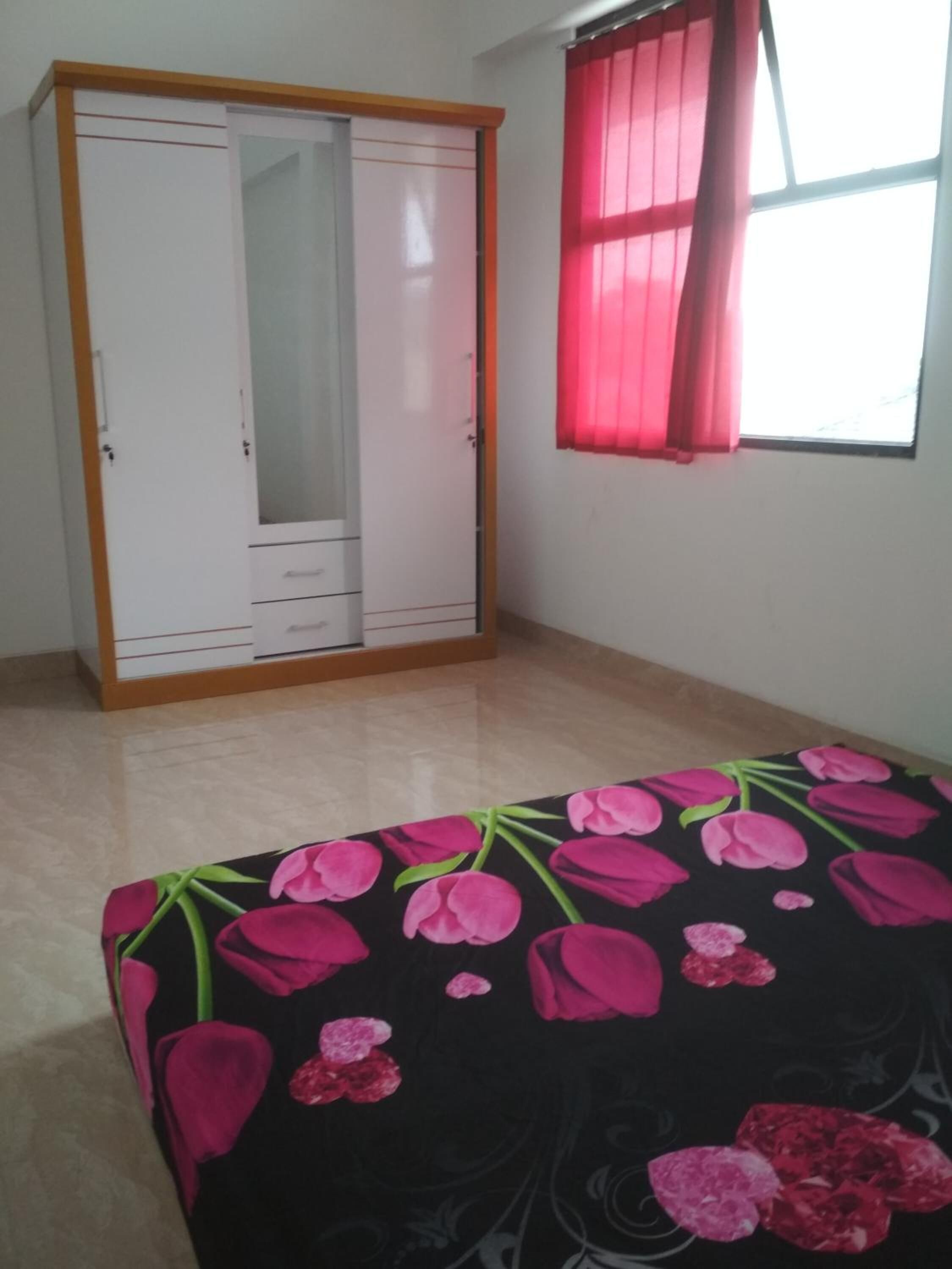 Un dormitorio con un armario, una cama con colcha estampada y una ventana con cortinas rojas.