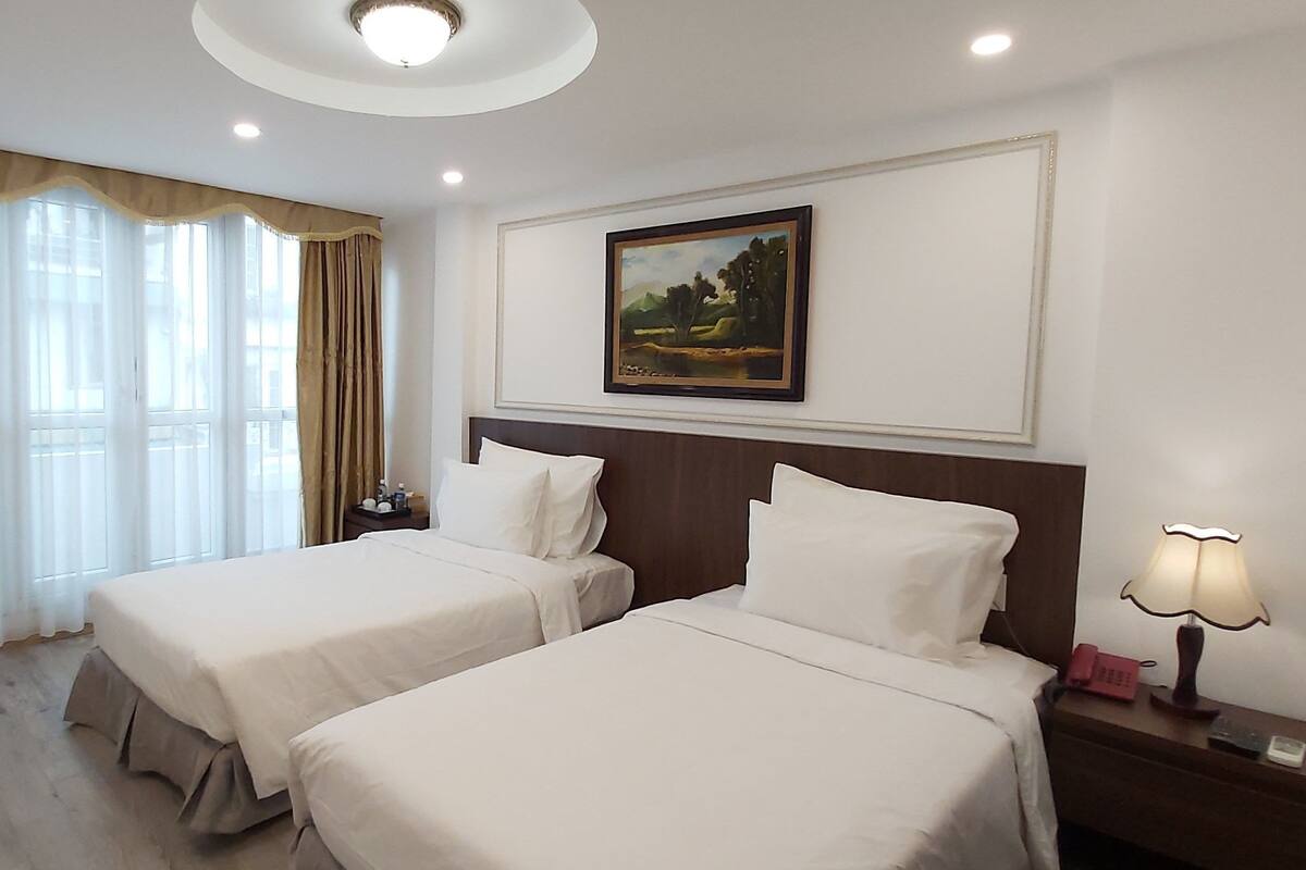 A hotel room with two beds, a painting on the wall, a bedside lamp, and a telephone on the nightstand.