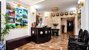 A hotel reception area with a marble floor, a reception desk, and a wall with clocks and posters.