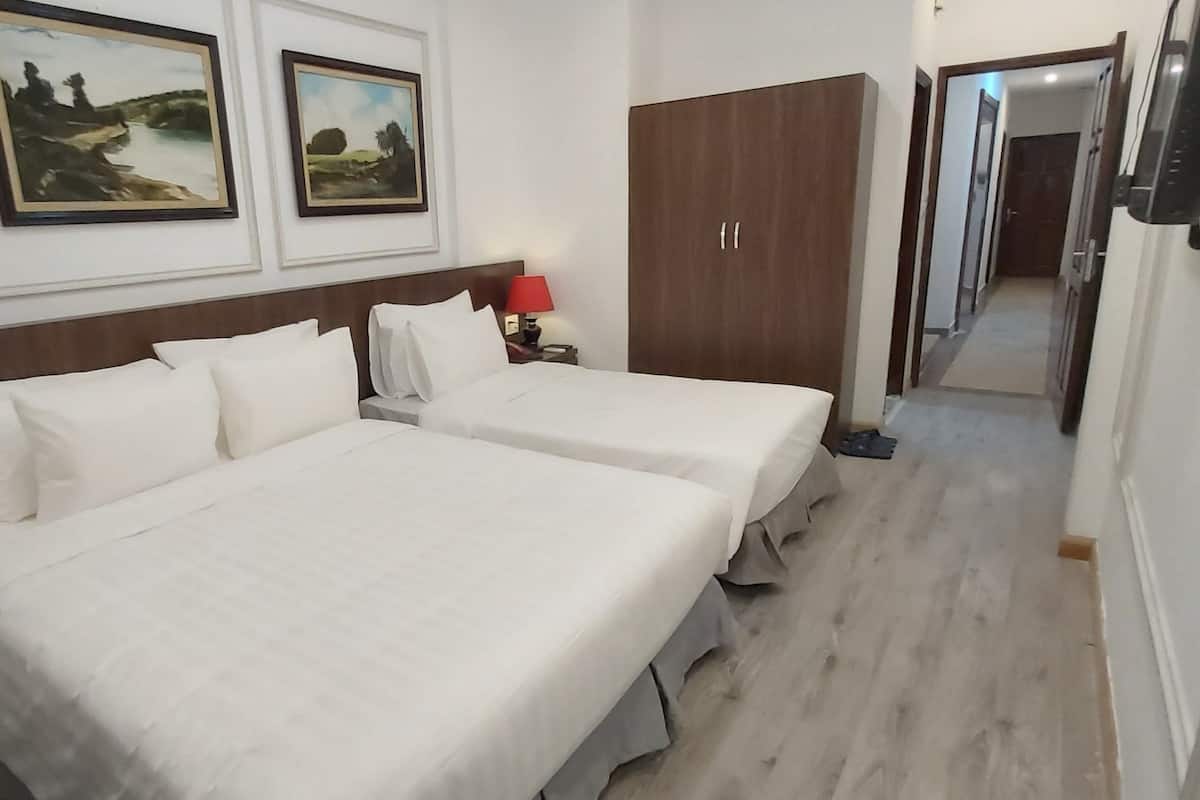 A hotel room with two beds, a wooden wardrobe, a nightstand with a lamp, and two framed landscape paintings on the wall.