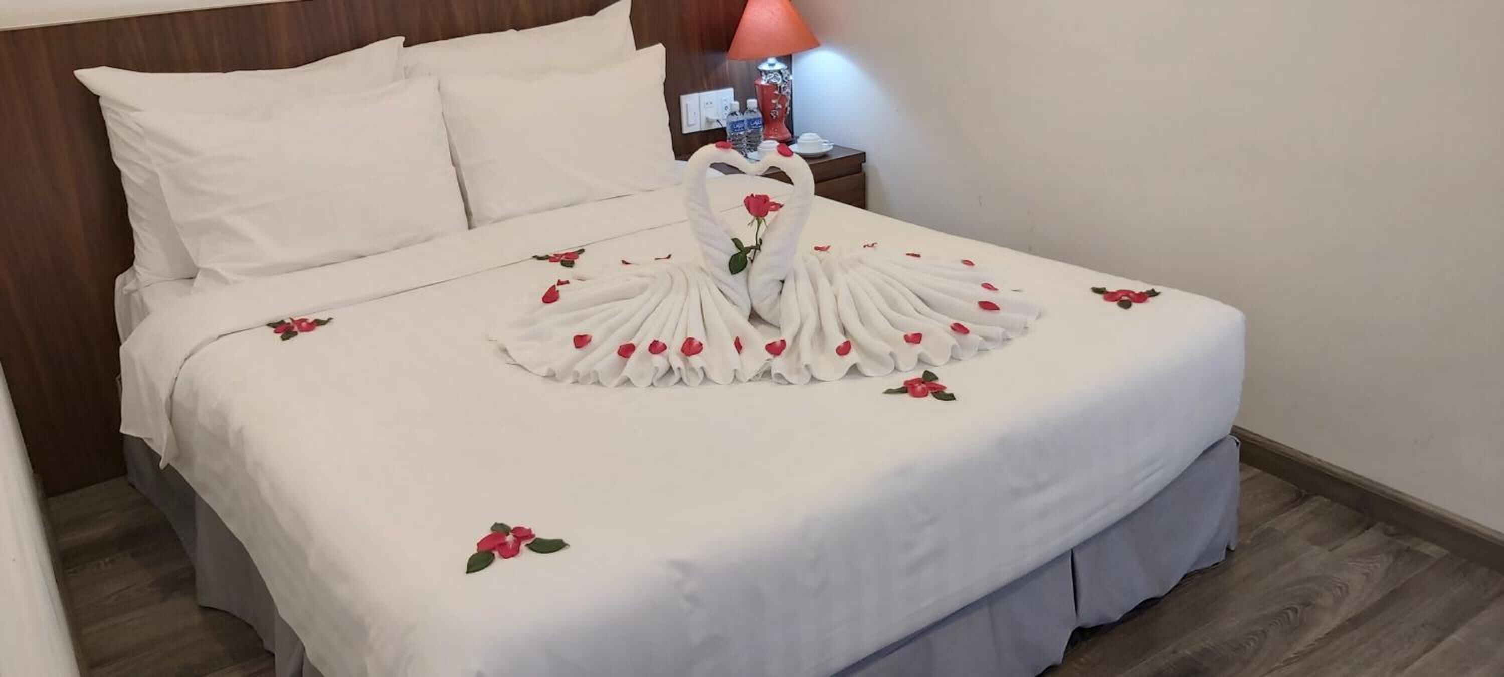 A neatly made bed with a swan-shaped towel and rose petals.