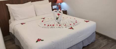 A neatly made bed with a swan-shaped towel and rose petals.