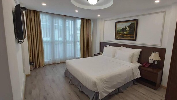 Habitación de hotel con una cama grande, una mesita de noche con lámpara, un cuadro en la pared y una ventana con cortinas.