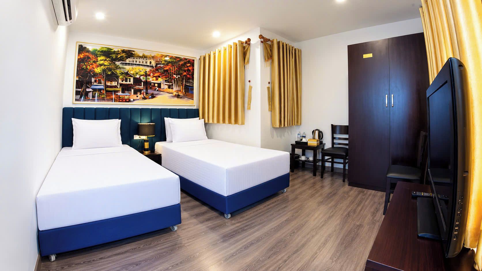A hotel room with two beds, a desk, a chair, a television, and a painting on the wall.