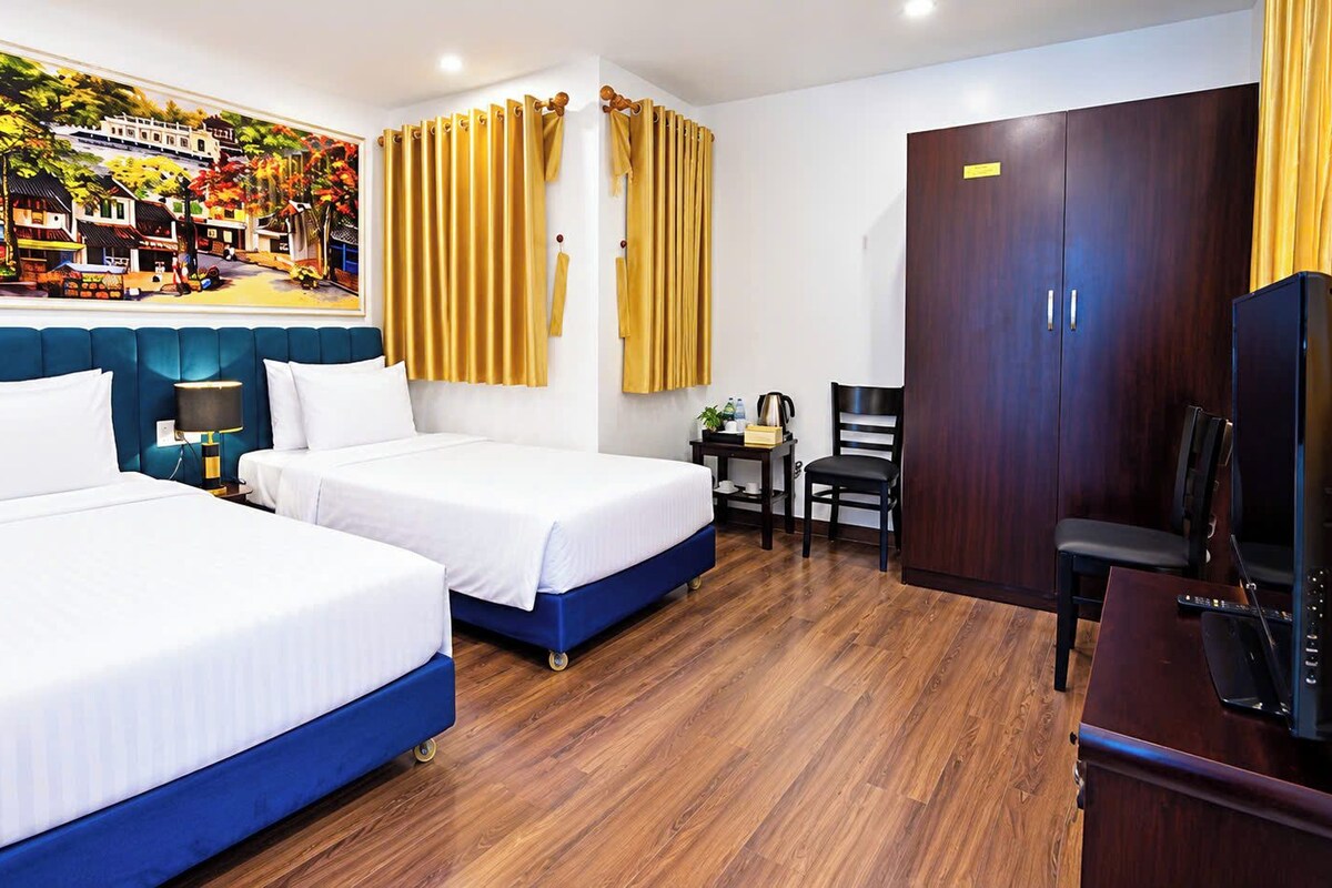 A hotel room with two beds, a desk, a chair, a television, and a painting on the wall.