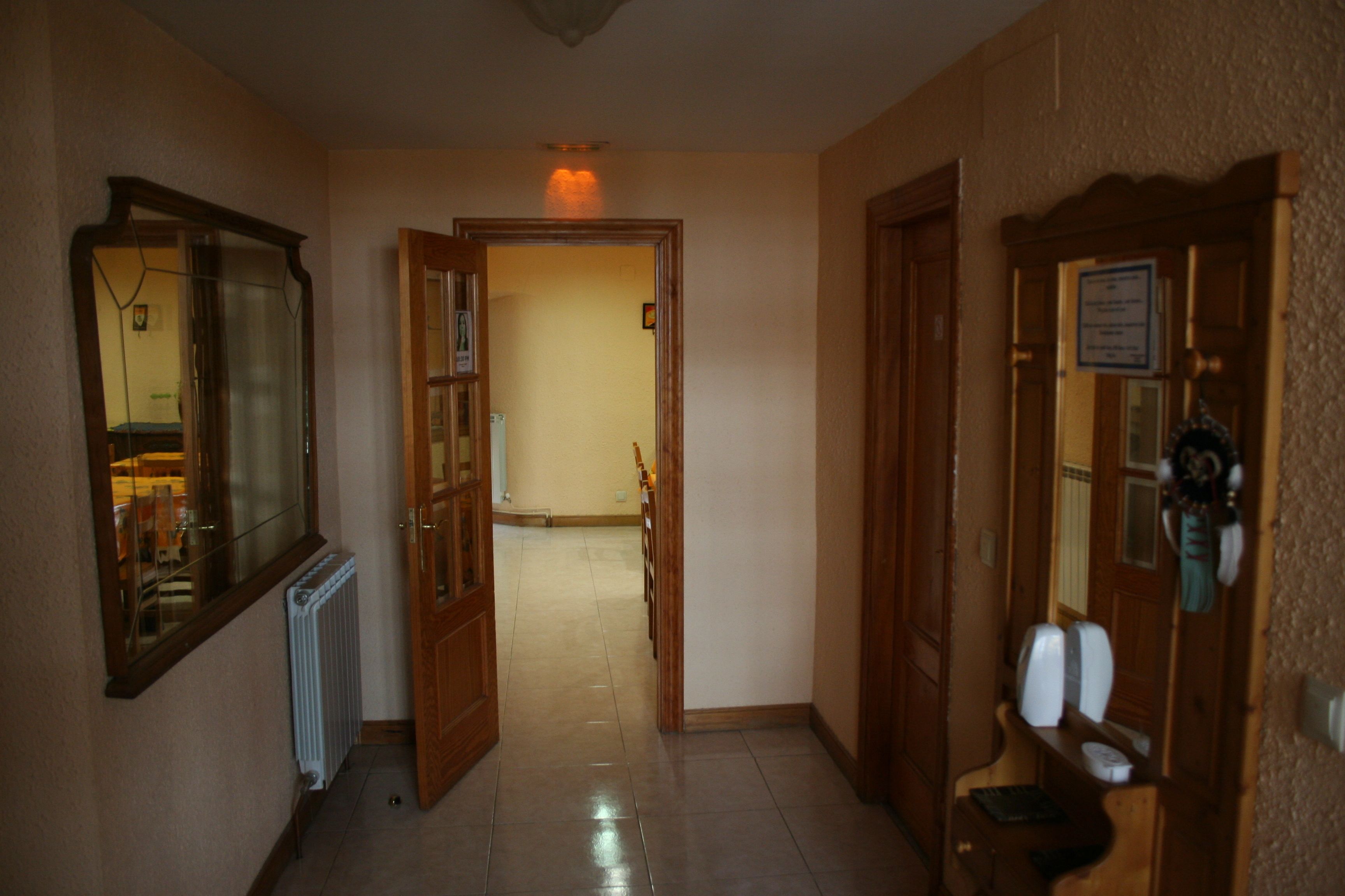 Un pasillo con una puerta de madera, un radiador y un espejo en la pared izquierda.