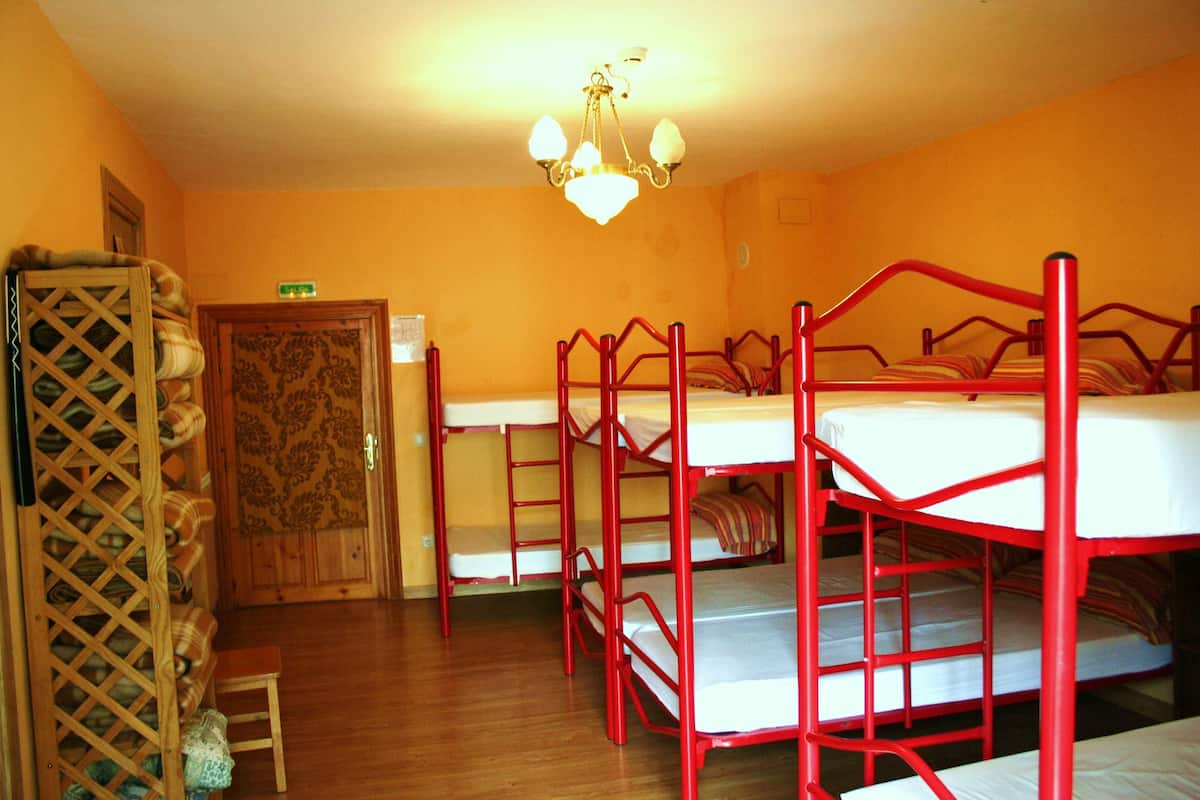 A dormitory room with bunk beds, a wooden door with a floral pattern, and a chandelier.