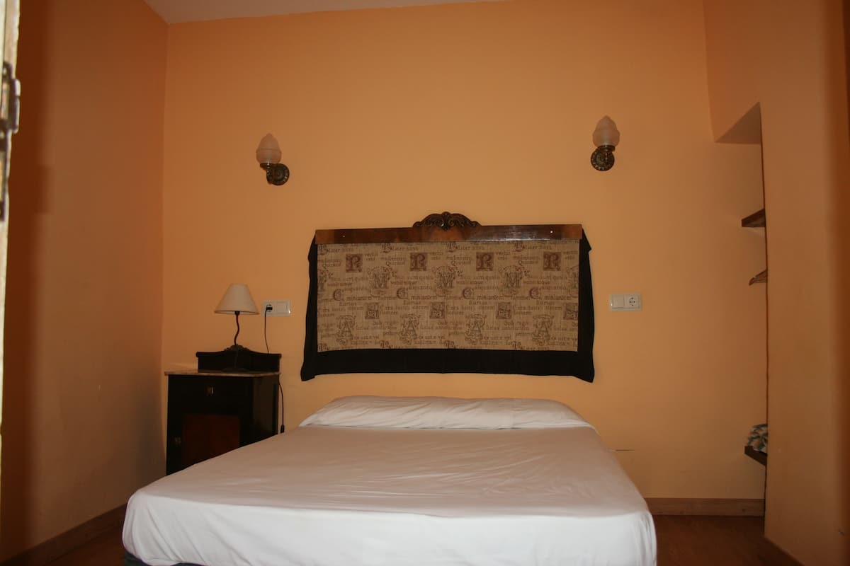 A hotel room with a bed, a nightstand, and two wall-mounted lamps.