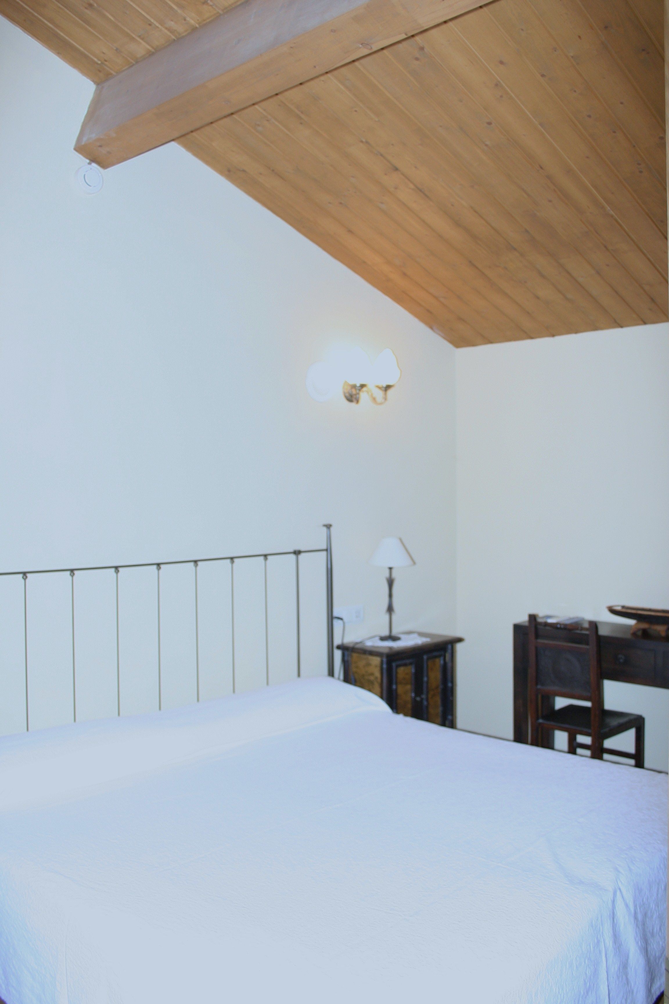 A bedroom with a bed, a desk, a chair, and a wall-mounted lamp.