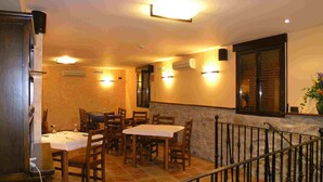 A dining area with wooden tables and chairs, a stone wall, and a staircase with a metal railing.