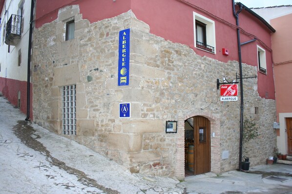 A stone building with a blue sign reading "ALBERGUE" and a door. - La Bodega Del Camino - Hostel (Valle de Yerri)