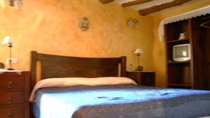 A bedroom with a wooden bed, a dresser, a television on a shelf, and a lamp on the dresser.