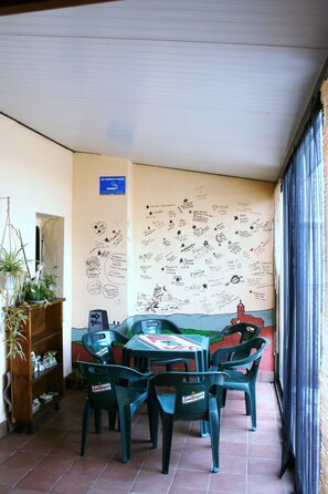 A covered patio area with a table and chairs, a wall with various writings and drawings, and a sign indicating a smoking area. - La Bodega Del Camino - Hostel (Valle de Yerri)