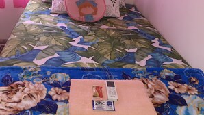 A bed with a floral bedspread, a pink pillow, and a folded towel with a phone and a ZINC product. - Almira Homestay near Airport - Hostel (Jambi)