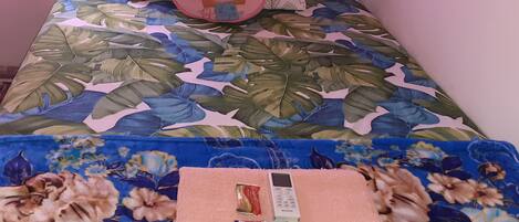A bed with a floral bedspread, a pink pillow, and a folded towel with a phone and a ZINC product.