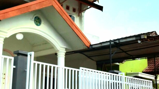 A house with a porch, a white railing, and a green sign. - Almira Homestay near Airport - Hostel (Jambi)