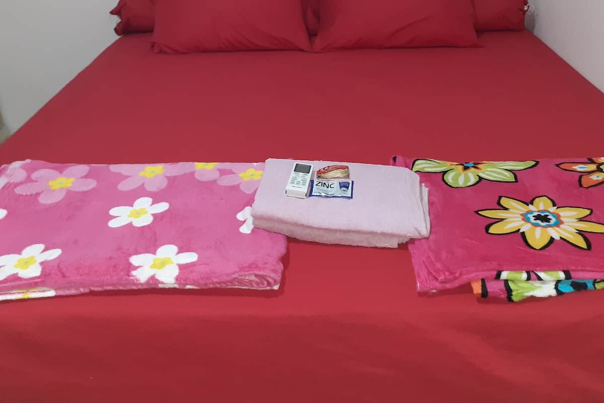 A bed with red bedding, a pink floral blanket, and a pink towel.