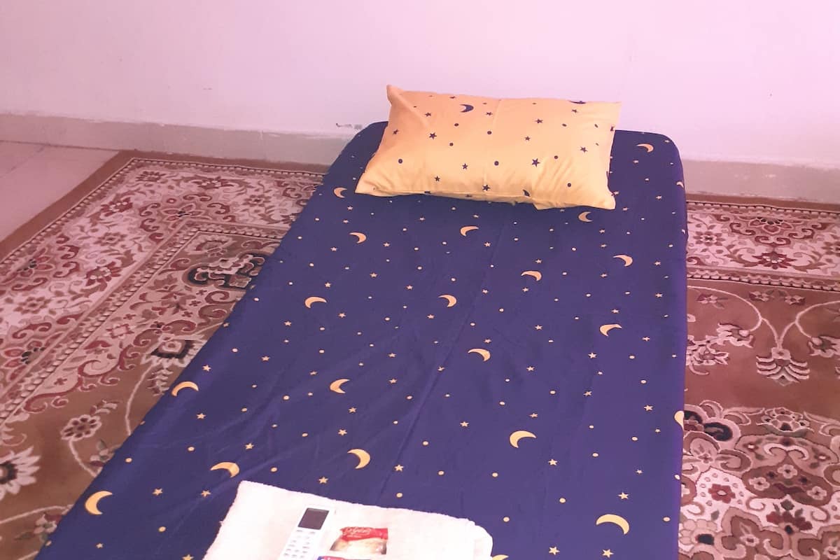 A single bed with a blue sheet featuring a star and crescent pattern, a white blanket, and a pillow with a star pattern.