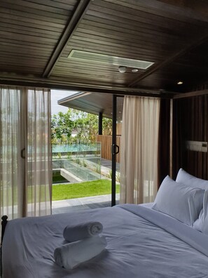 Een slaapkamer met een groot bed, uitzicht op een zwembad en een schuifdeur naar een buitenruimte.