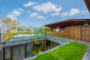 Een modern gebouw met een glazen atrium, een houten terras en een gazon.