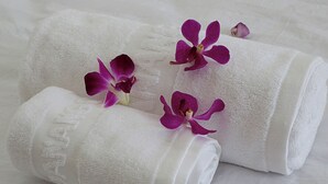 Dos toallas enrolladas blancas con flores púrpuras sobre una superficie blanca con textura.