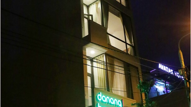 Un hotel llamado 'danang beach2' con diseño moderno, que cuenta con un llamativo letrero de neón y una entrada visible.