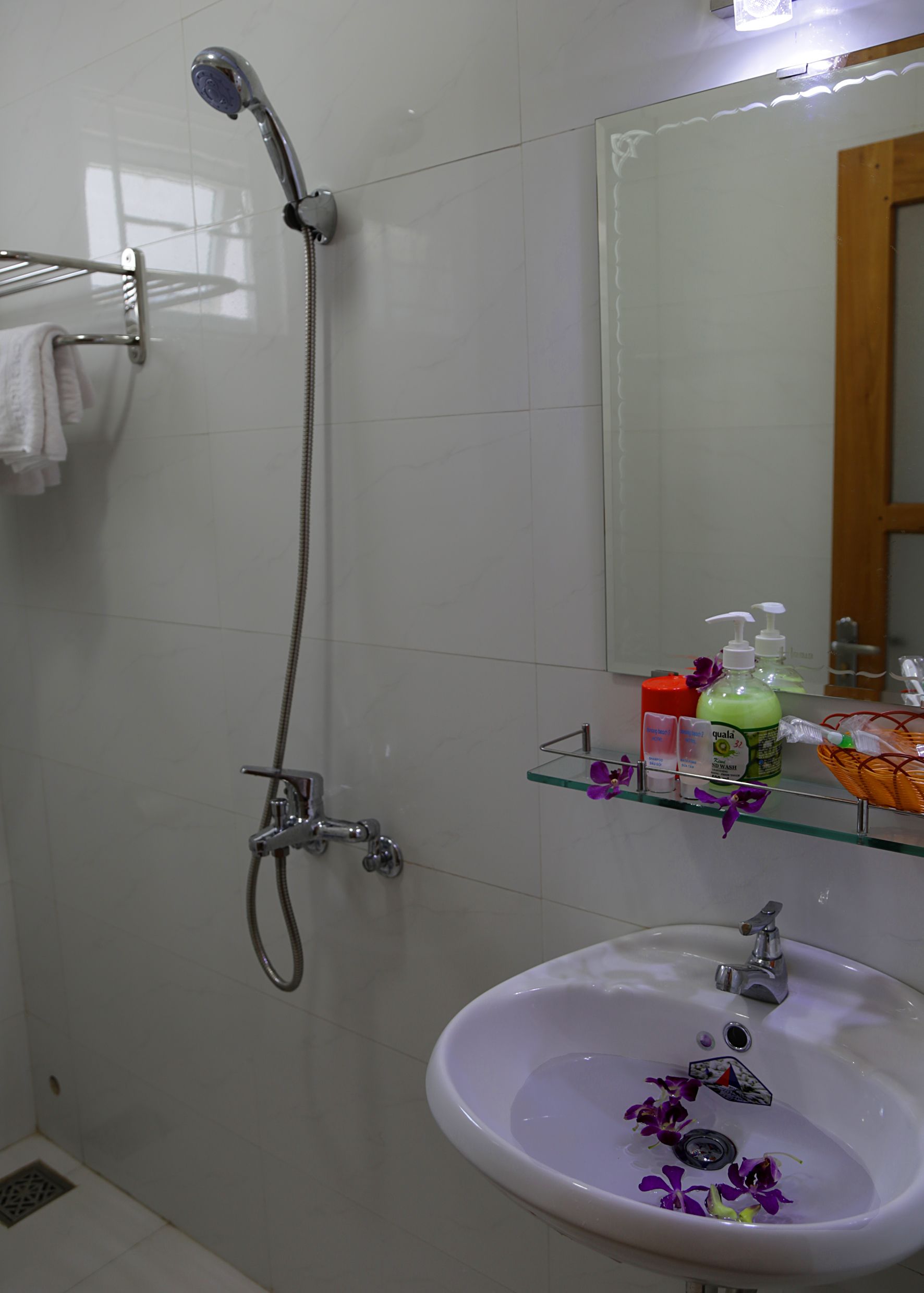 A bathroom with a shower, a sink, and a glass shelf with toiletries.