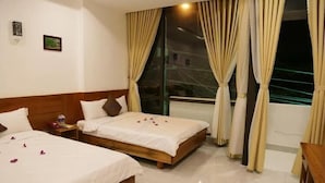 Habitación de hotel con dos camas, cortinas color crema, vista nocturna desde la ventana y cabecera de madera.