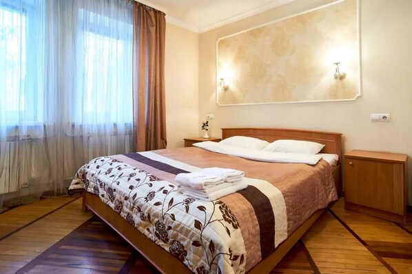 Relax in this serene hotel room featuring a large bed, wooden nightstand, and wall-mounted light fixture.