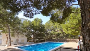 A rectangular swimming pool with clear blue water, surrounded by trees and a stone wall. - Apartment Rits by Interhome (Salou)