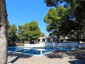 A swimming pool area with a white building in the background, surrounded by trees. - Apartment Rits by Interhome (Salou)