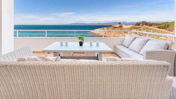 A balcony with wicker furniture, a table, and a view of the sea and mountains. - Apartment Rits by Interhome (Salou)