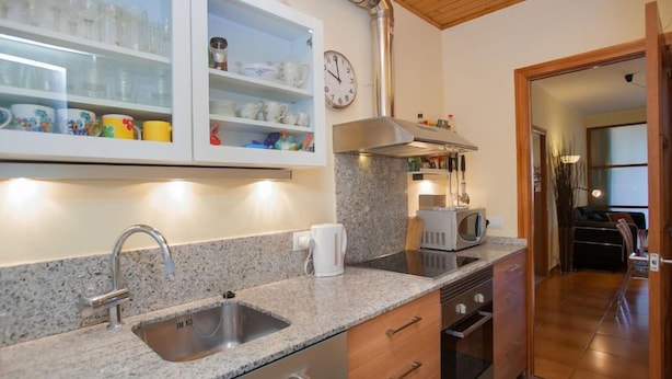 A kitchen with granite countertops, a stainless steel sink, wooden cabinets, a microwave, and a clock on the wall. - Sardenya - Casp by Interhome (Barcelona)