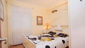 A bedroom with a bed, a bedside table, a lamp, a framed picture on the wall, and a door with a curtain. - Sardenya - Casp by Interhome (Barcelona)