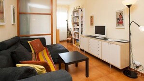 A living room with a sofa, a small table, a bookshelf, a TV, and a lamp. - Sardenya - Casp by Interhome (Barcelona)