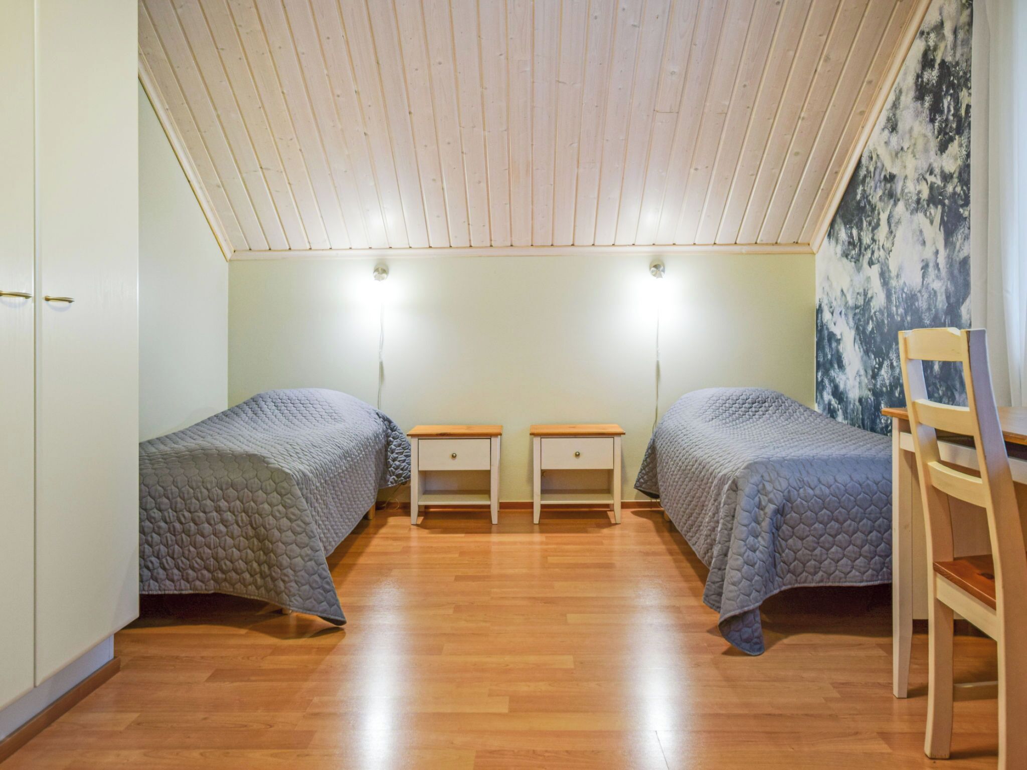 Habitación con dos camas, piso de madera, una silla y un cuadro en la pared.