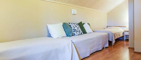 A room with two single beds, wooden flooring, and a sloped ceiling.