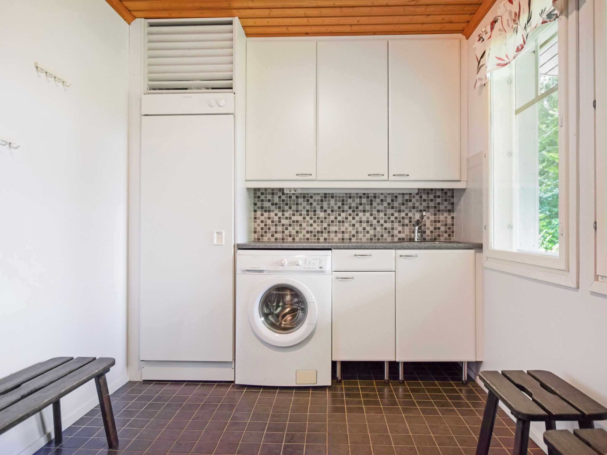Una cocina compacta con lavadora incorporada, un ventanal pequeño y un banco.