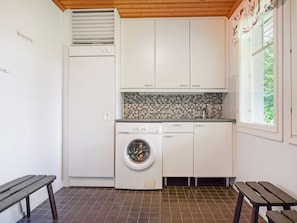 Una cocina compacta con lavadora incorporada, un ventanal pequeño y un banco.