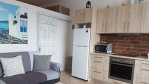 A compact living space with a kitchenette, a sofa with cushions, a small table with snacks, and a painting on the wall. - The Stone House Naxos (Naxos)