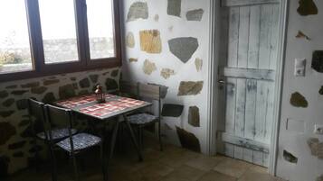 A small room with a stone wall, a wooden door, a table with a checkered tablecloth, and two chairs.