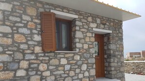 A stone building with a wooden door and window, featuring a stone facade and steps leading to the entrance. - The Stone House Naxos (Naxos)