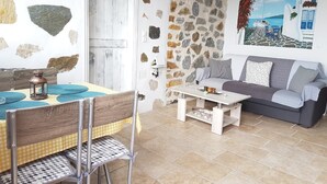 A room with a stone wall, a wooden door, a dining table with chairs, a sofa, and a painting of a coastal scene. - The Stone House Naxos (Naxos)