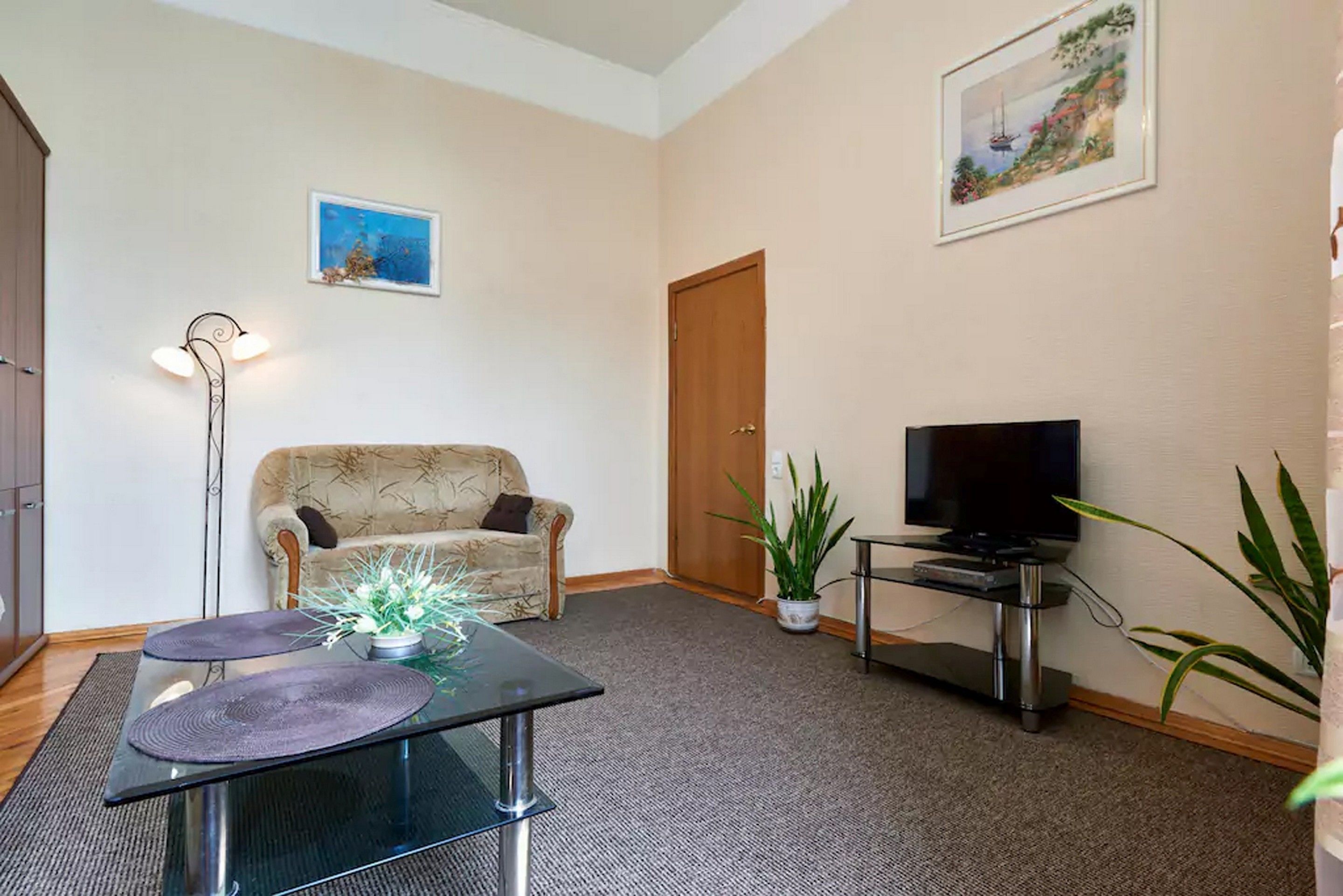 A living room with a sofa, a glass coffee table, a TV on a stand, and a door.