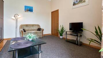 A living room with a sofa, a glass coffee table, a TV on a stand, and a door.